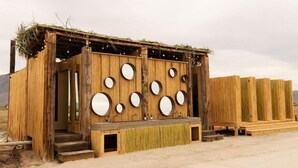 A rustic wooden structure with multiple circular mirrors on the front wall, a small entrance, and a thatched roof. - ENDEMICA GLAMP RESORT (Cuatro Cienegas)
