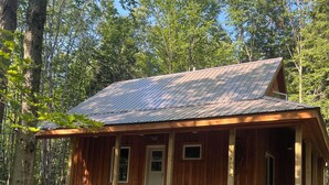 Une cabane en bois rustique, surmontée d’un toit en métal, entourée d’arbres et située sur un terrain rocheux.
