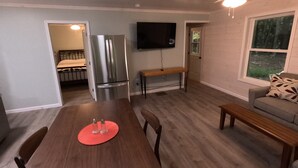 Un vaste espace de vie comprenant une table à manger en bois, un canapé et un téléviseur fixé au mur.