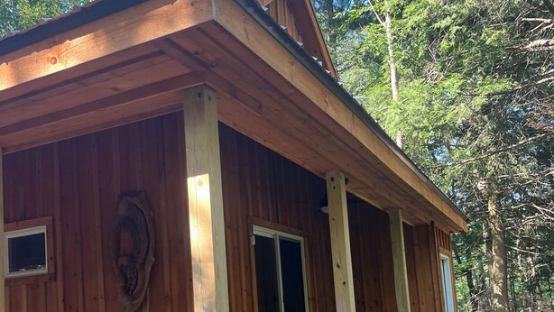 Une cabane en bois dotée d’un porche, de grandes fenêtres et d’un style rustique.