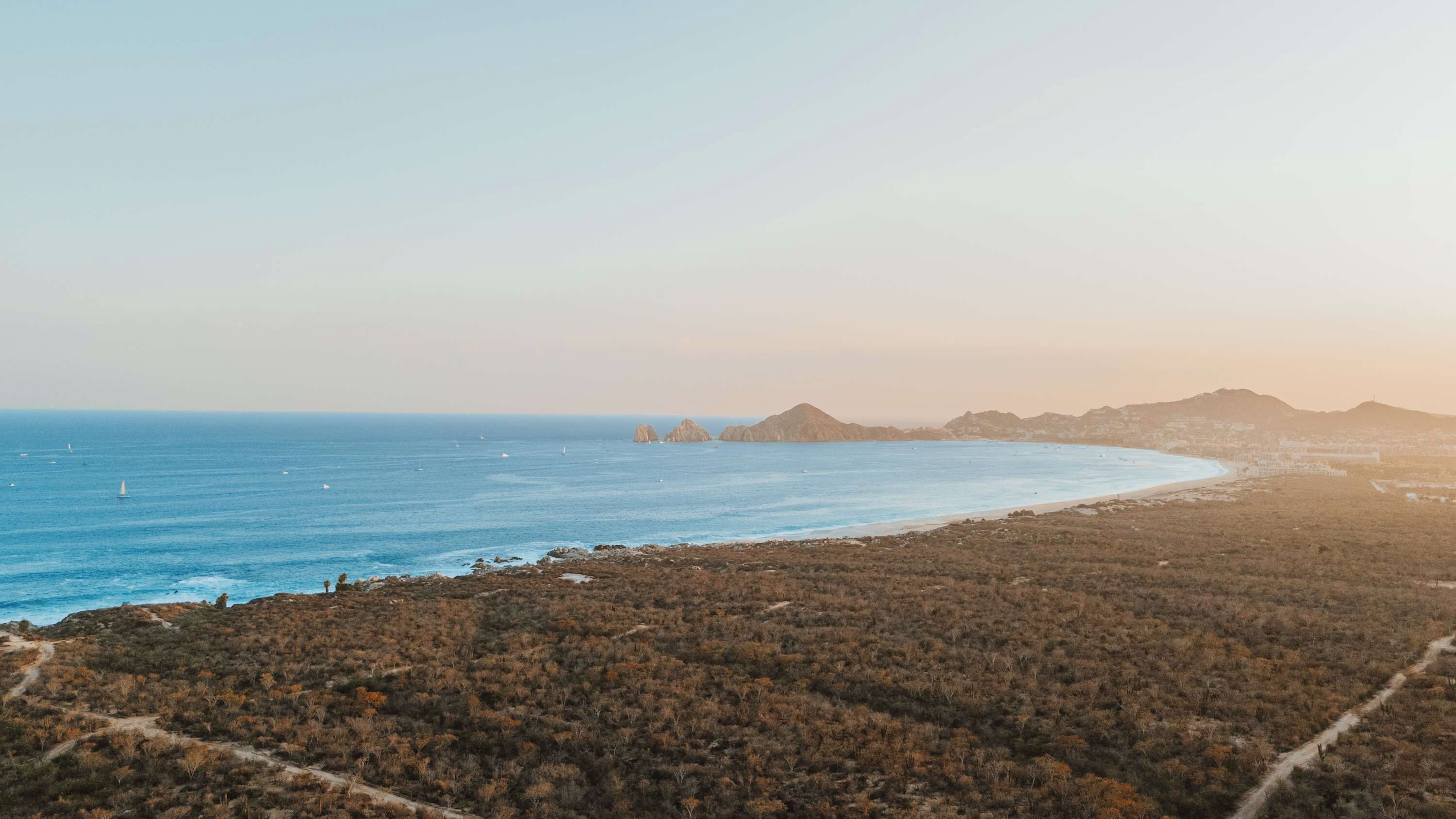 A coastal landscape with a beach, rocky terrain, and distant mountains.