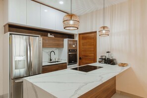 A modern kitchen with stainless steel appliances, a marble countertop, wooden cabinets, and two hanging light fixtures.
