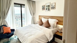 Una habitación de hotel moderna con una cama grande, vistas de la ciudad y un cuadro de un paisaje urbano en la pared.