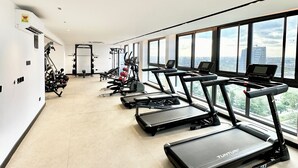 Un gimnasio con cintas de correr, máquinas de pesas y vistas a la ciudad a través de amplios ventanales.