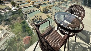 Un balcón con sillas de mimbre y una mesa de vidrio con vistas a un paisaje urbano que incluye edificios y un puente.