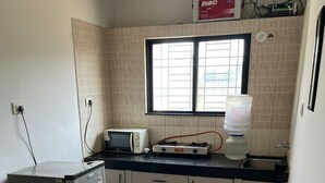 Eine kleine Küche mit Mikrowelle, Toaster und Wasserspender. Ein Glastisch und ein Stuhl sind vorhanden.