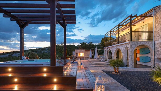A luxurious outdoor pool area with a wooden deck, stone walls, and a stone building with arched windows. - Villa Ventina with Pool (Senj)