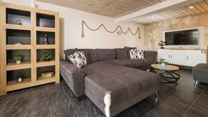 A modern living room with a sectional sofa, wooden shelving, a round coffee table, and a flat-screen TV mounted on a stone wall. - Villa Ventina with Pool (Senj)