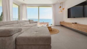 Un salon moderne avec un canapé d’angle, une table basse ronde et un téléviseur fixé au mur.