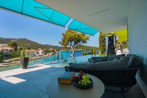 Ein moderner Außenbereich mit Sitzgelegenheit und Blick auf eine Küstenstadt sowie ein Infinity-Pool.