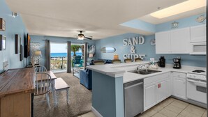 A kitchen with a central island, white cabinets, and a view of the ocean through a sliding door. - Pelican Isle 107 (Fort Walton Beach)