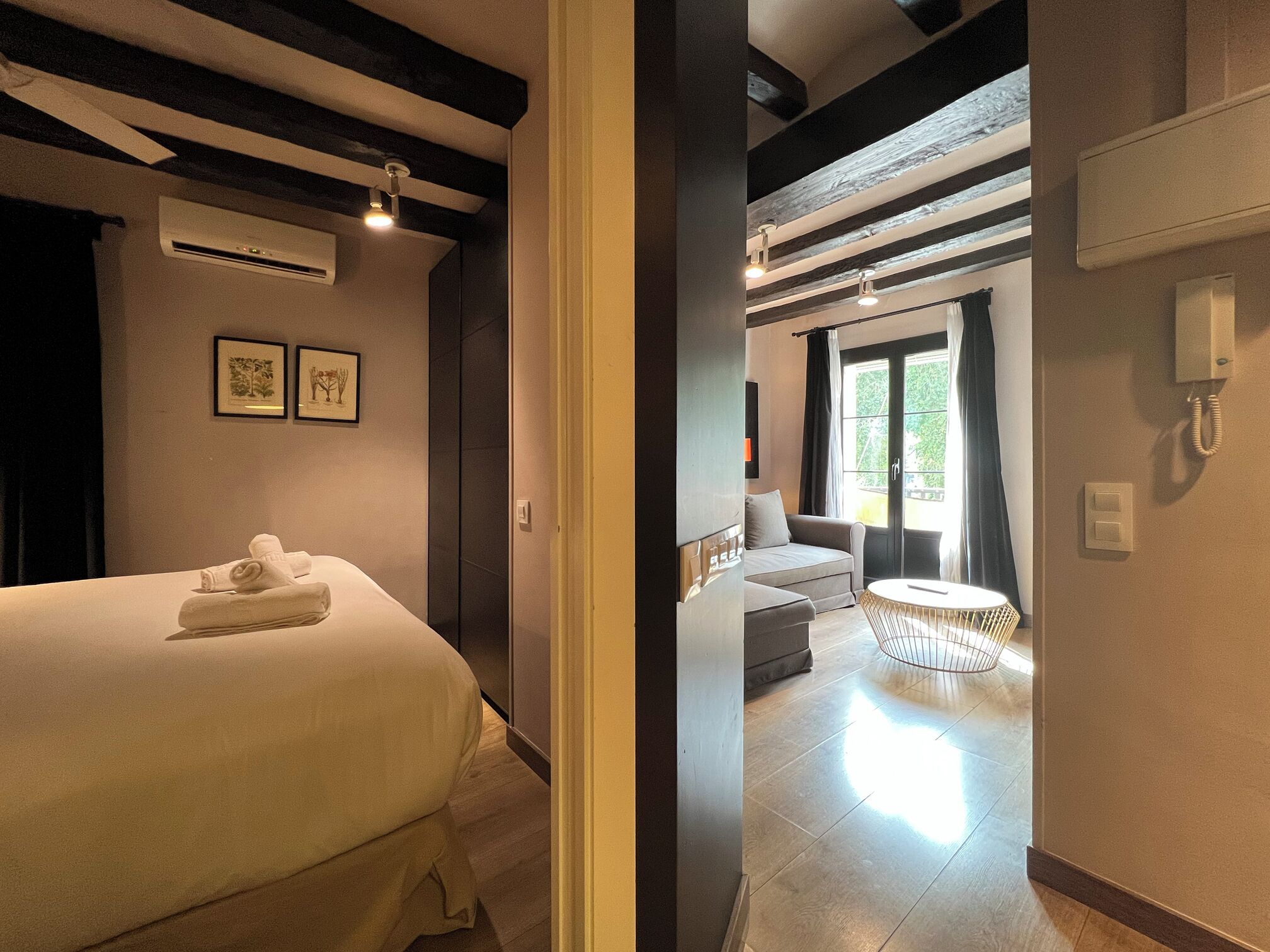 Una habitación de hotel moderna con una cama grande, un sofá y una pequeña mesa redonda. Hay una ventana con cortinas y vistas a zonas verdes.