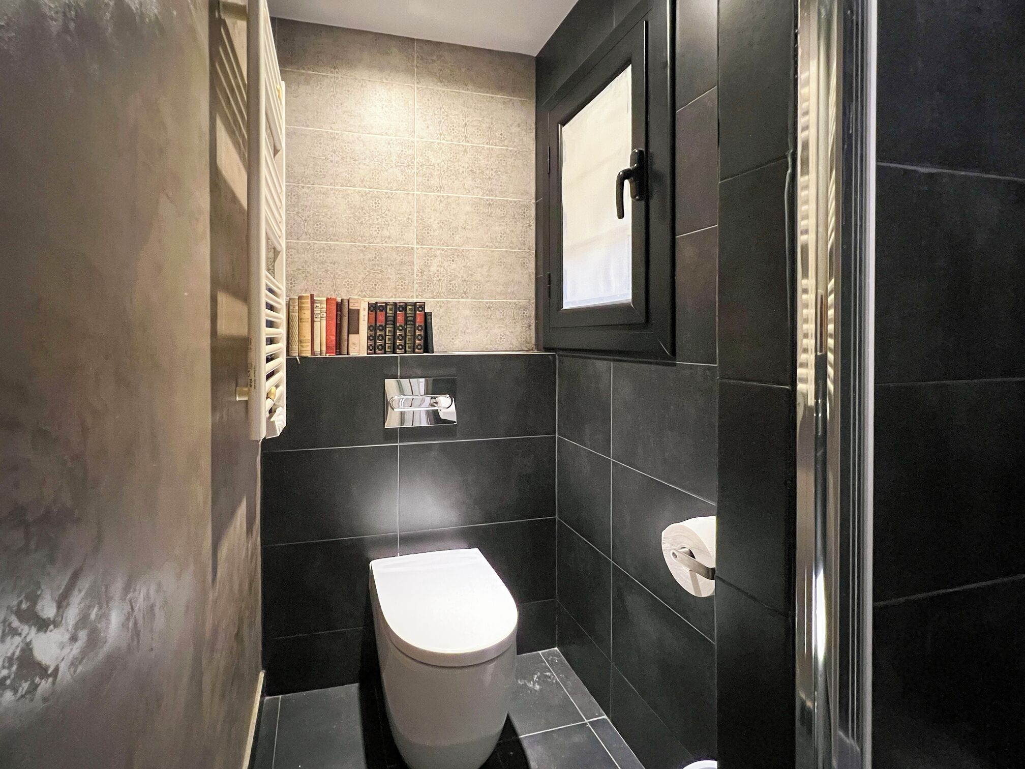 Een moderne badkamer met een toilet, een douchecabine van glas en een plank met boeken.