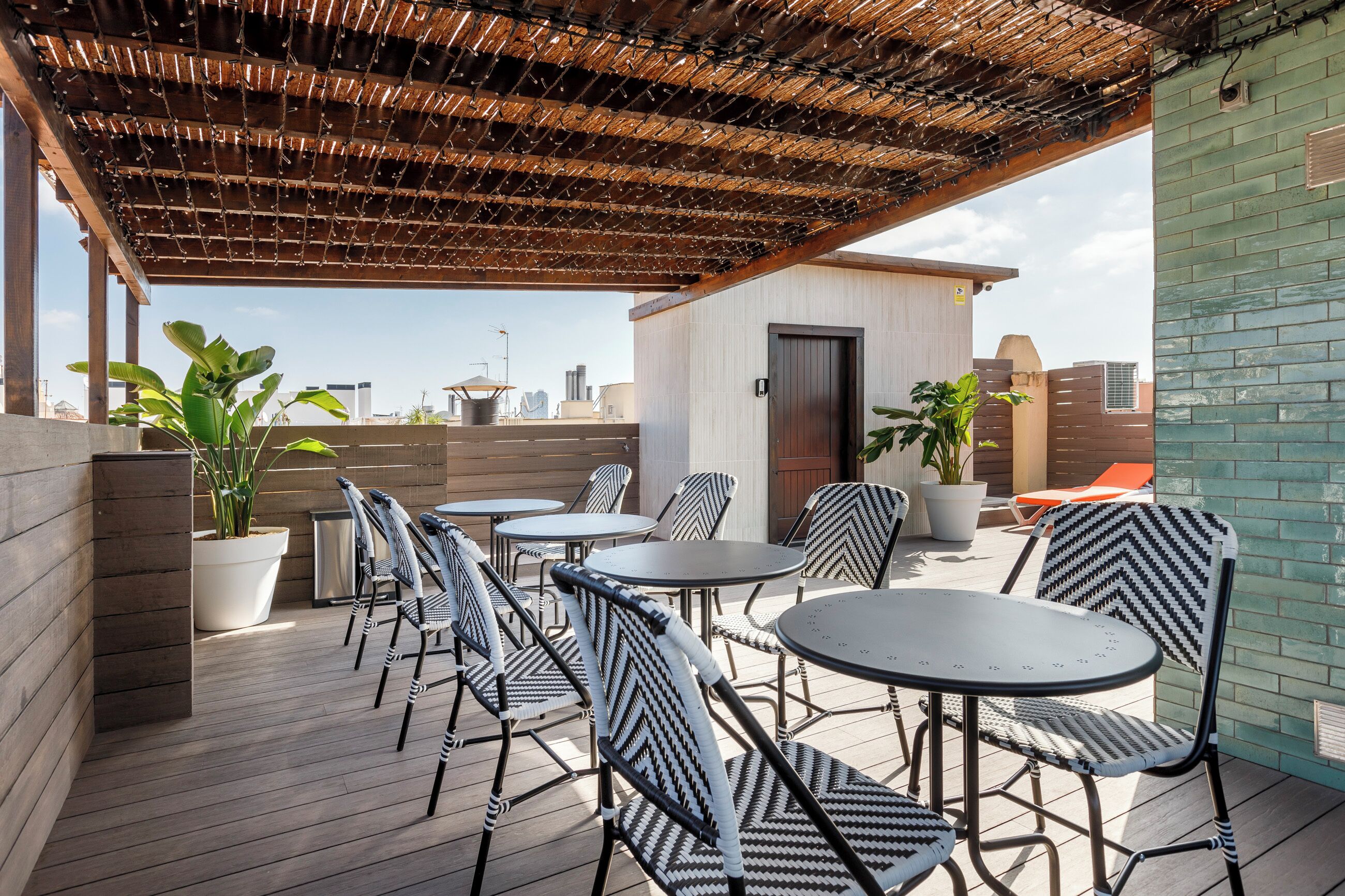 A rooftop patio with outdoor seating, potted plants, and a view of the city skyline.