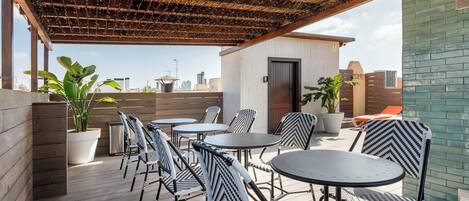 A rooftop patio with outdoor seating, potted plants, and a view of the city skyline.