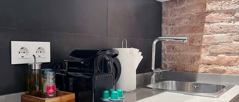 A modern kitchen with a black countertop, a built-in oven, a coffee machine, and a sink with a brick wall backsplash.