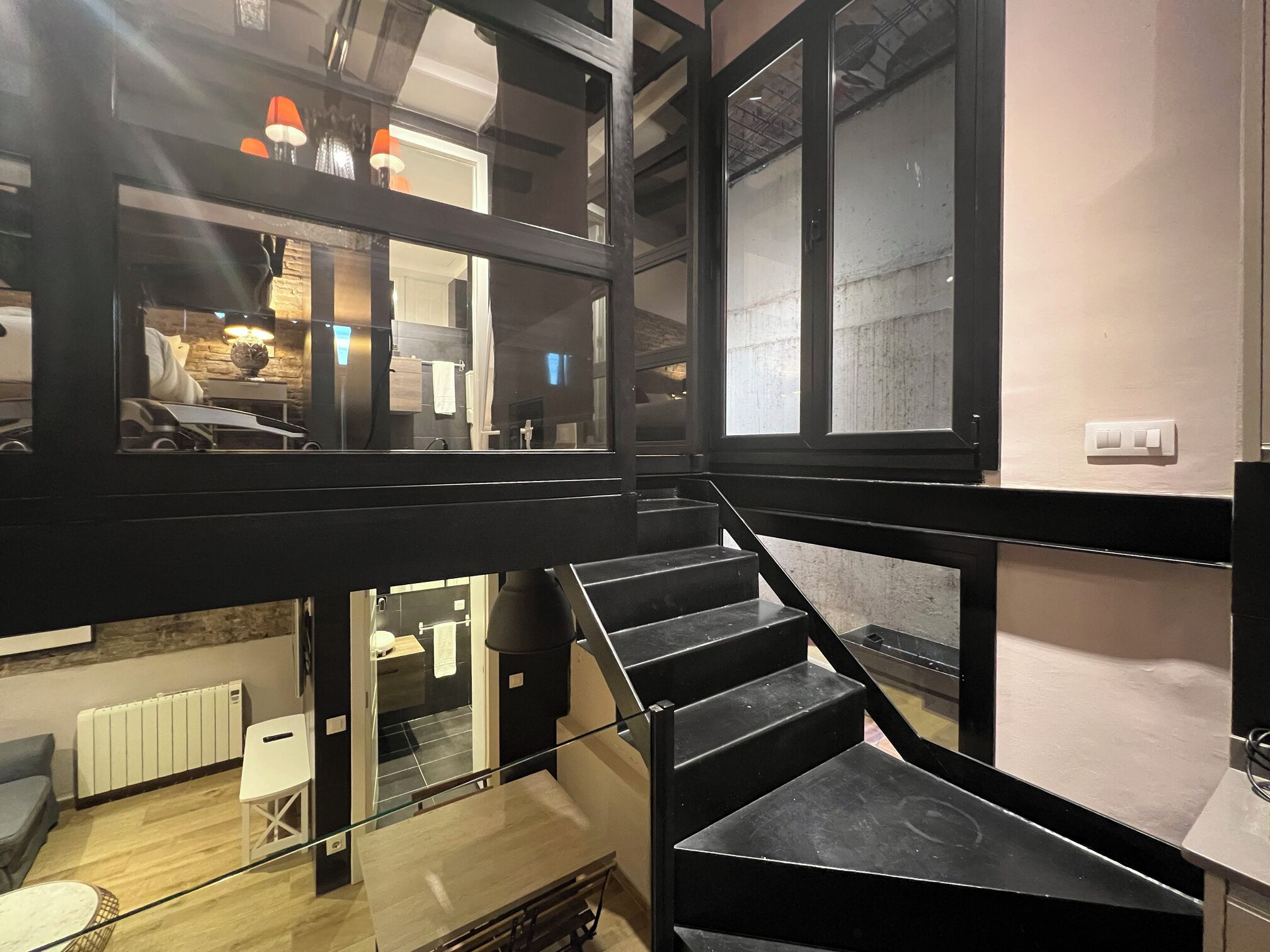 A modern interior with a staircase leading to an upper level, a glass railing, and a view of a kitchen area below.