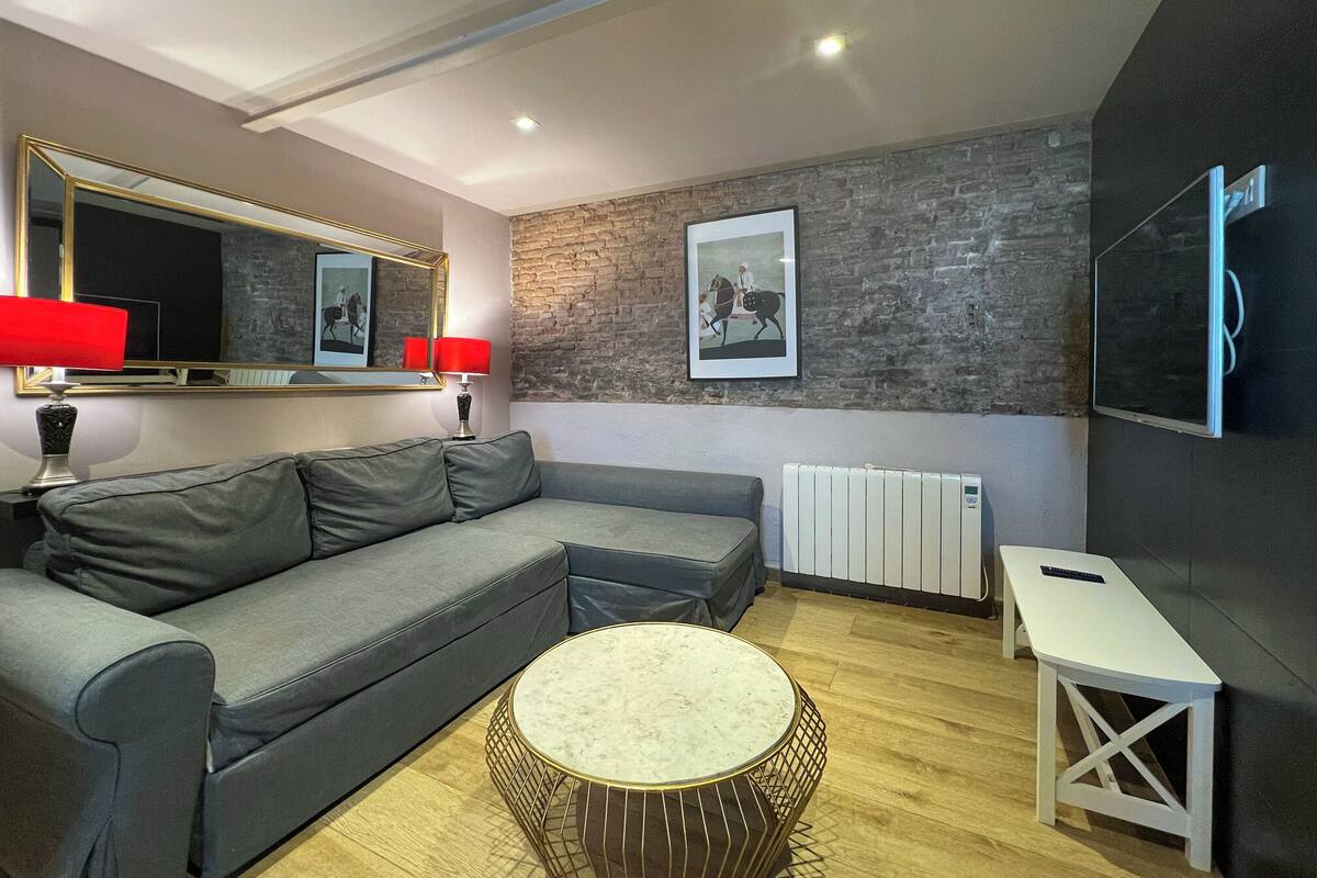 A modern living room with a grey sofa, a round coffee table, a red floor lamp, a framed picture on the wall, and a television mounted on the wall.