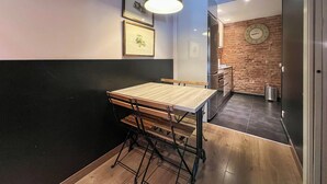 Un comedor con una mesa y sillas de madera, una lámpara colgante, cuadros en la pared y una pared de ladrillo con un reloj.