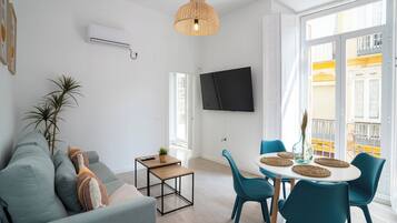 A modern living room with a sofa, a small table, and a dining area with chairs.