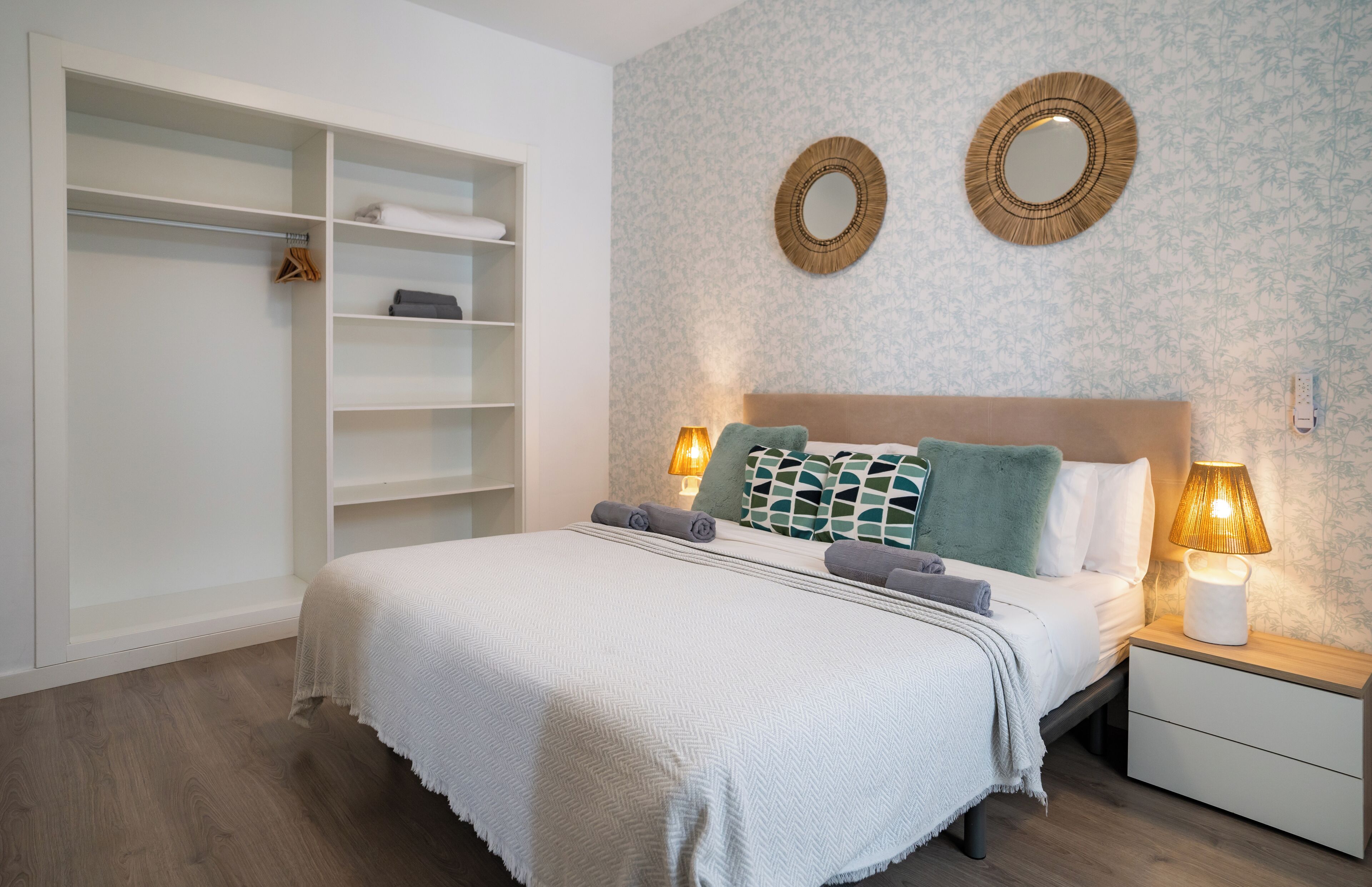 A bedroom with a bed, bedside lamps, a nightstand, a wardrobe, and two wall mirrors.
