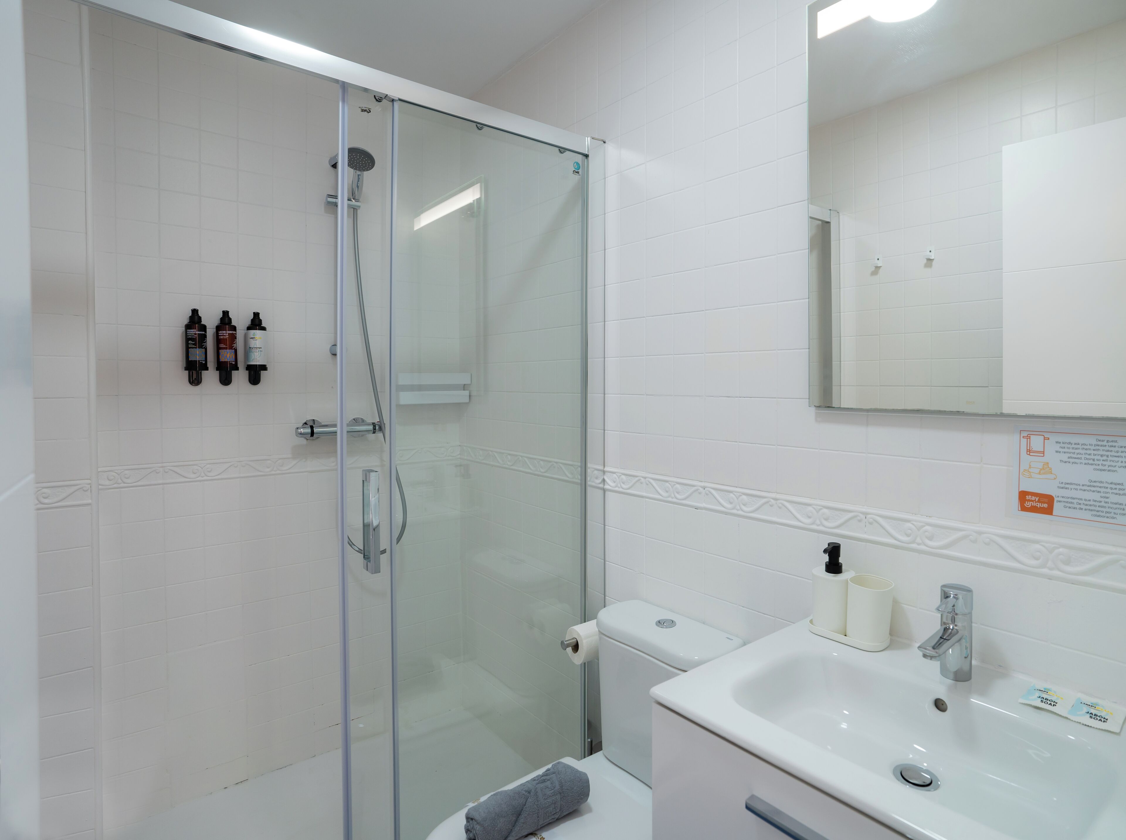 Un baño moderno con ducha envuelta en vidrio, un lavamanos blanco y un espejo.