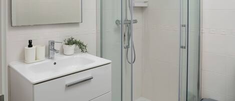 A modern bathroom with a glass-enclosed shower, a white vanity with drawers, a mirror, and a small potted plant.