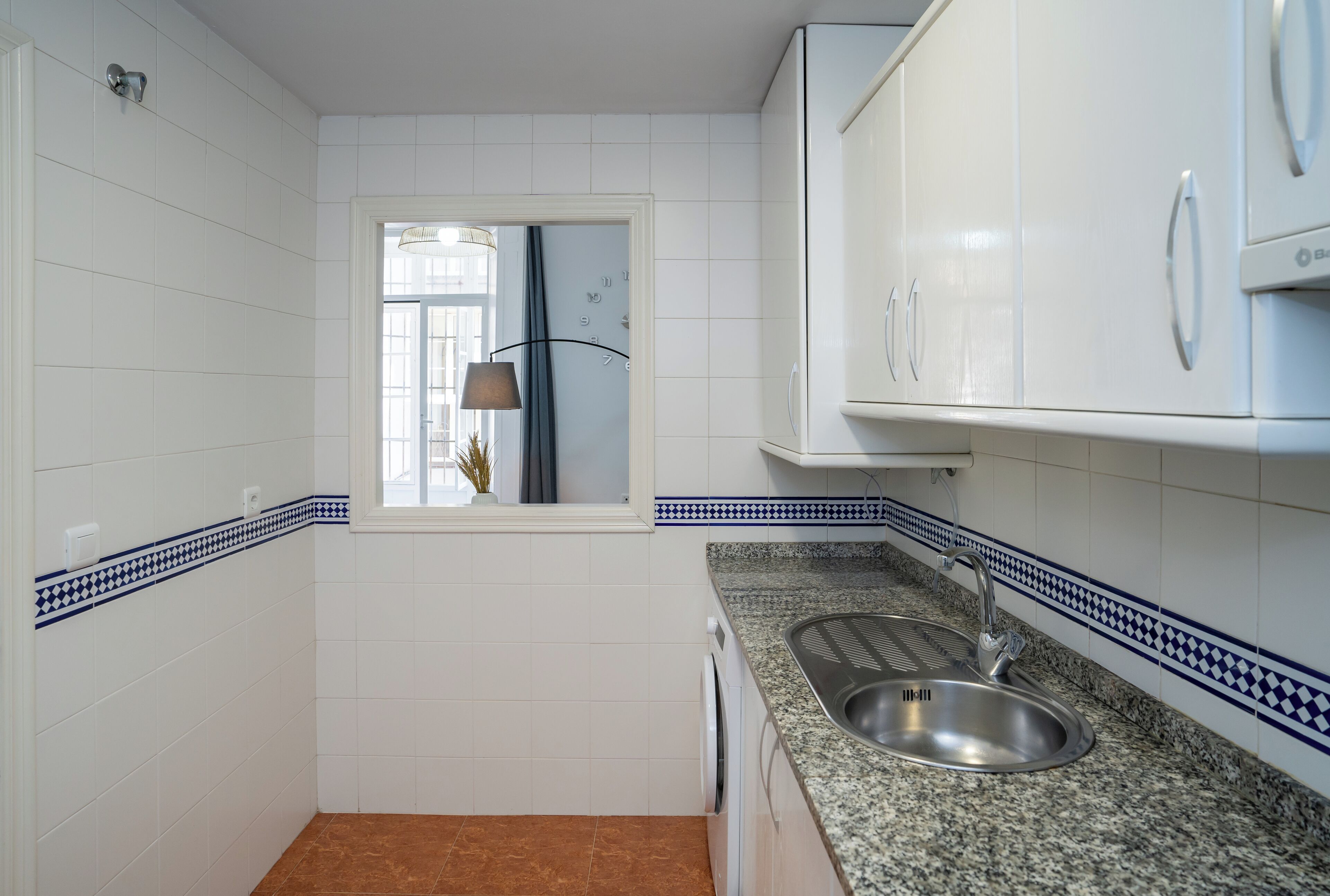 Una cocina compacta con gabinetes blancos, encimera de granito y un lavamanos.