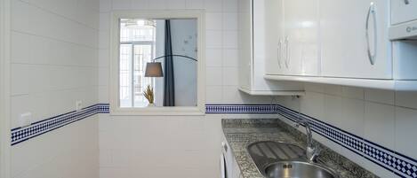 Una cocina compacta con gabinetes blancos, encimera de granito y un lavamanos.