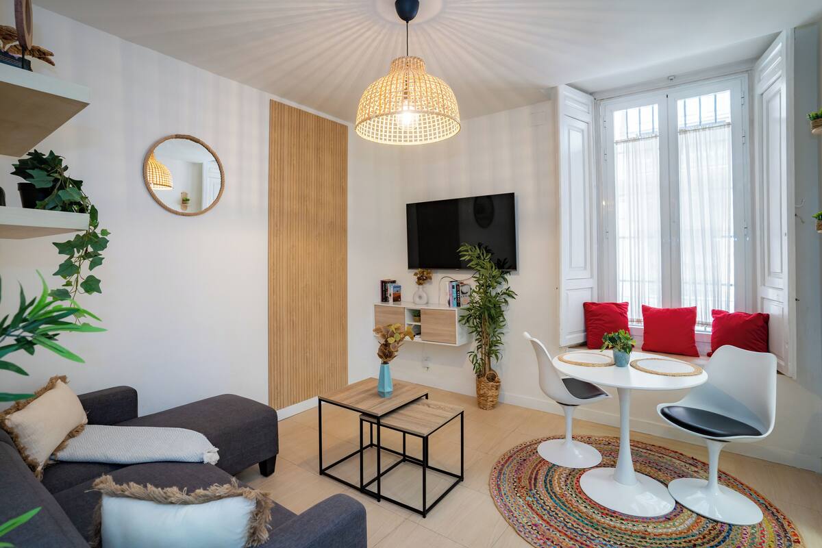 Ein modernes Wohnzimmer mit einer Couch, einem kleinen Tisch, einem Fernseher und einem Fenster mit Vorhängen.