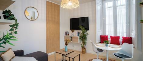 Una sala de estar moderna con un sofá, una mesita, un televisor y una ventana con cortinas.