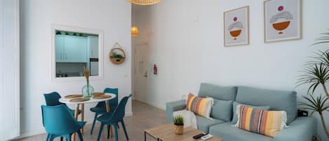 Una sala de estar moderna con sillas color turquesa, un sofá azul claro, una mesa de centro de madera y una lámpara colgante.
