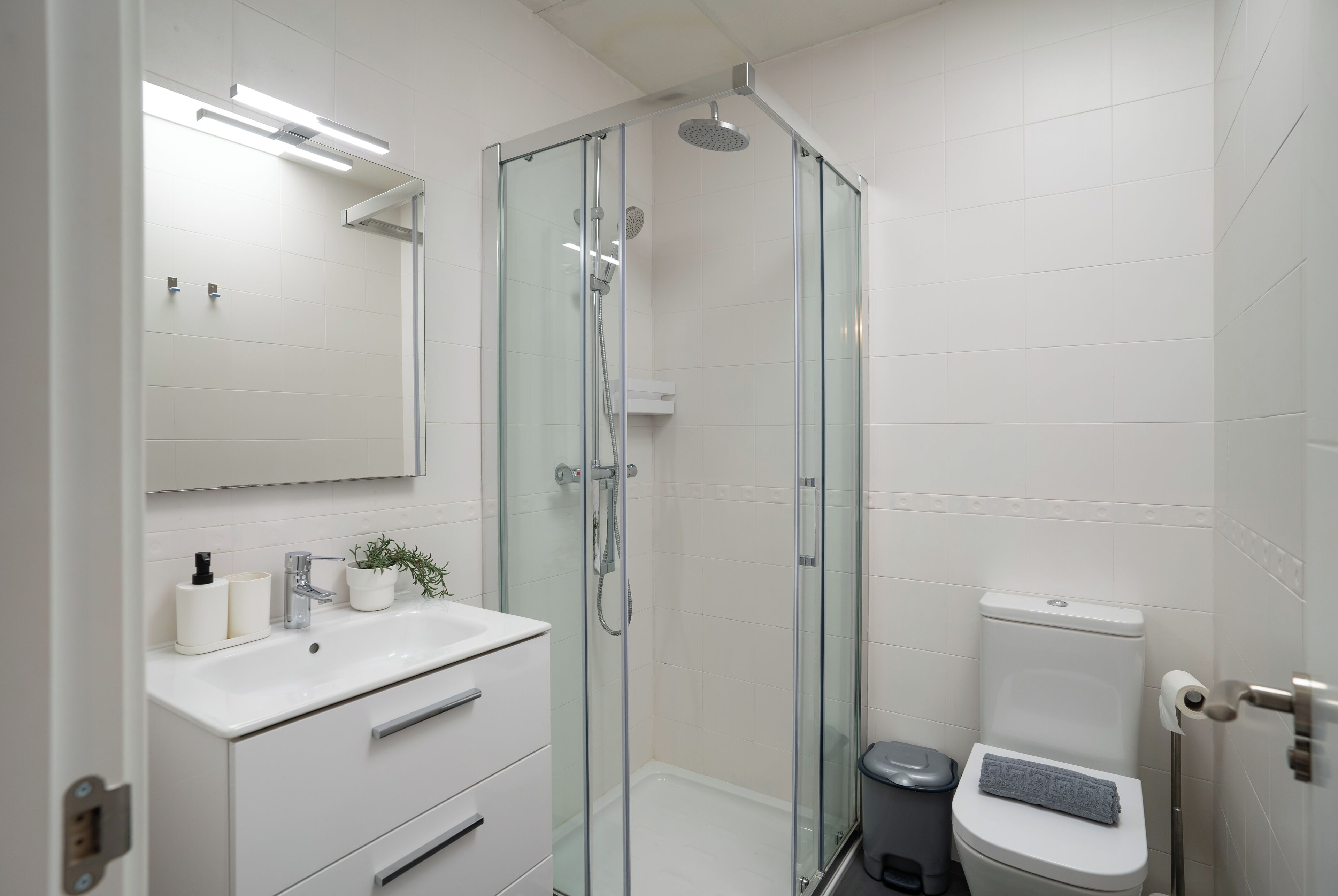 A modern bathroom with a glass-enclosed shower, a white sink with a plant, and a toilet with a towel on top.