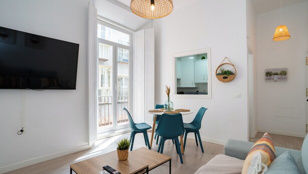 Ein modernes Wohnzimmer mit Flachbildfernseher, einem Essbereich mit rundem Tisch und Stühlen sowie einer Couch mit Decke.