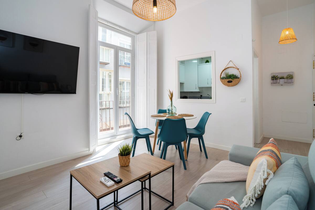Ein modernes Wohnzimmer mit Flachbildfernseher, einem Essbereich mit rundem Tisch und Stühlen sowie einer Couch mit Decke.