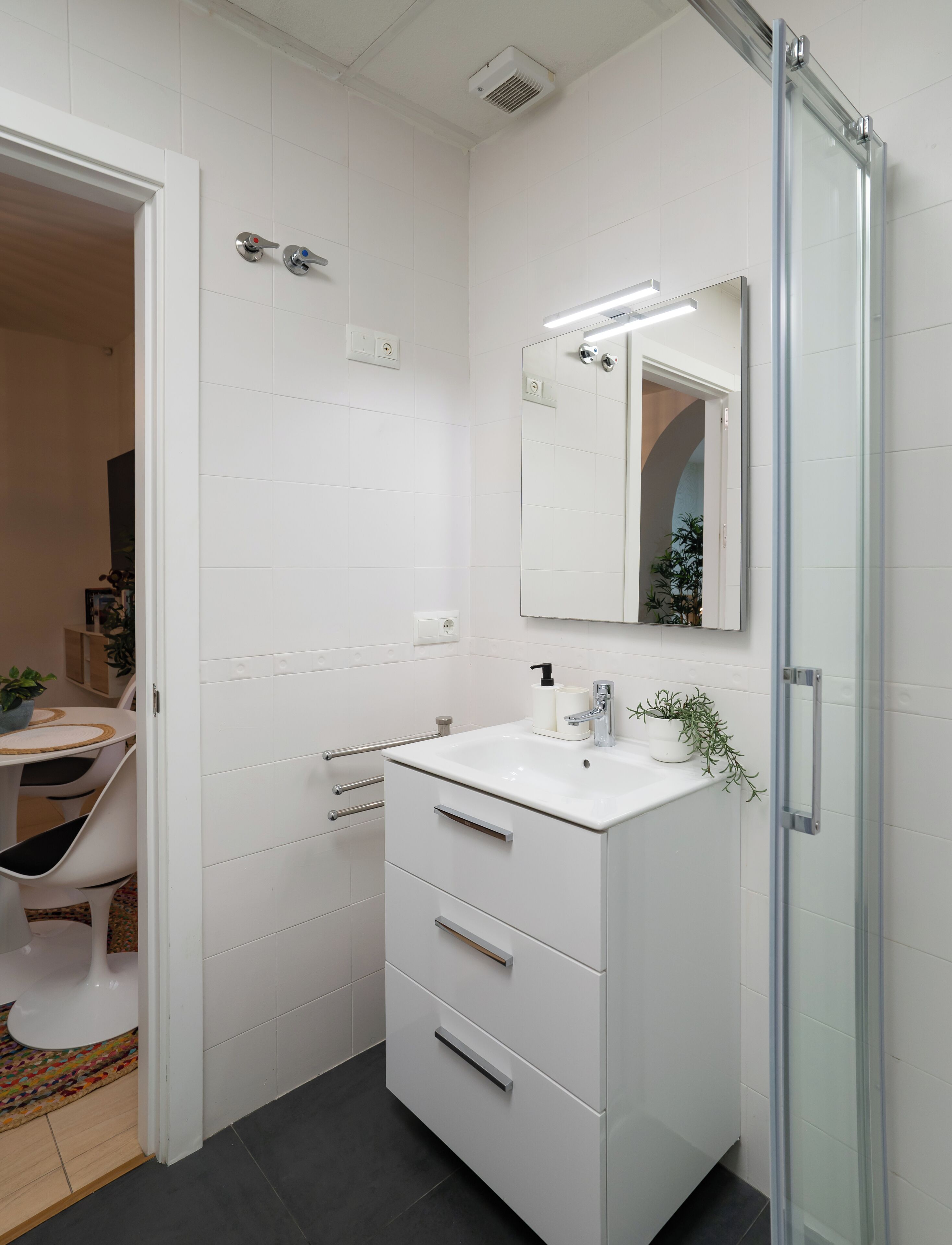 A modern bathroom with a white vanity, a glass shower enclosure, and a mirror.