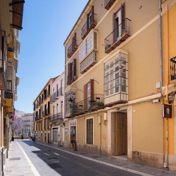 A street with multi-story buildings, balconies, and a clear sky.
