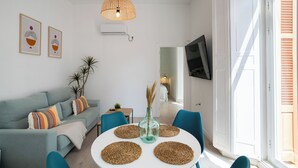 Ein modernes Wohnzimmer mit einem hellblauen Sofa, Türkis-Stühlen, einem weißen Tisch mit gewobenen Untersetzern, einer Korbtropflicht und einem Fernseher an der Wand.