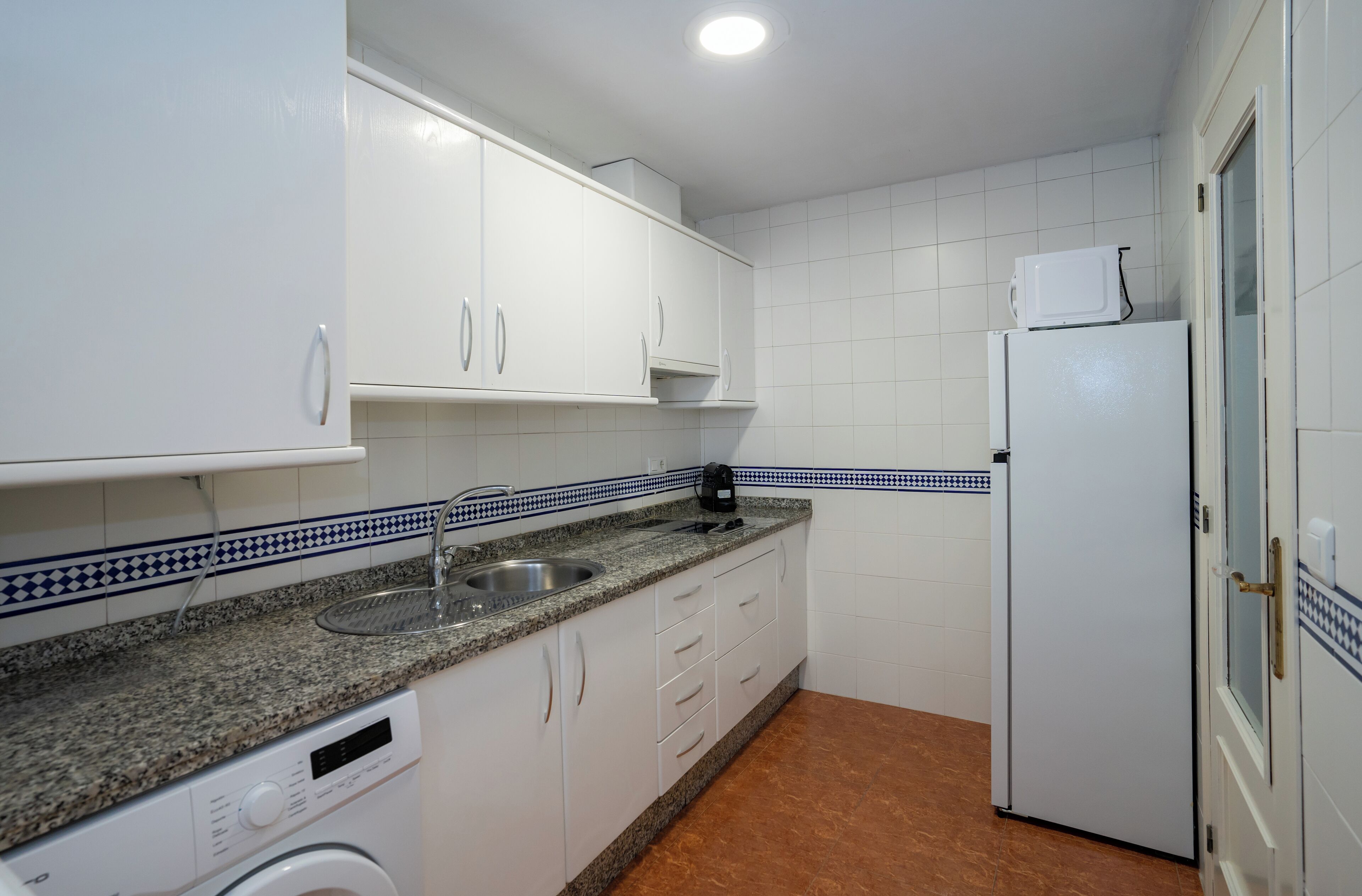 A compact kitchen with white cabinets, a granite countertop, a built-in dishwasher, and a white refrigerator.