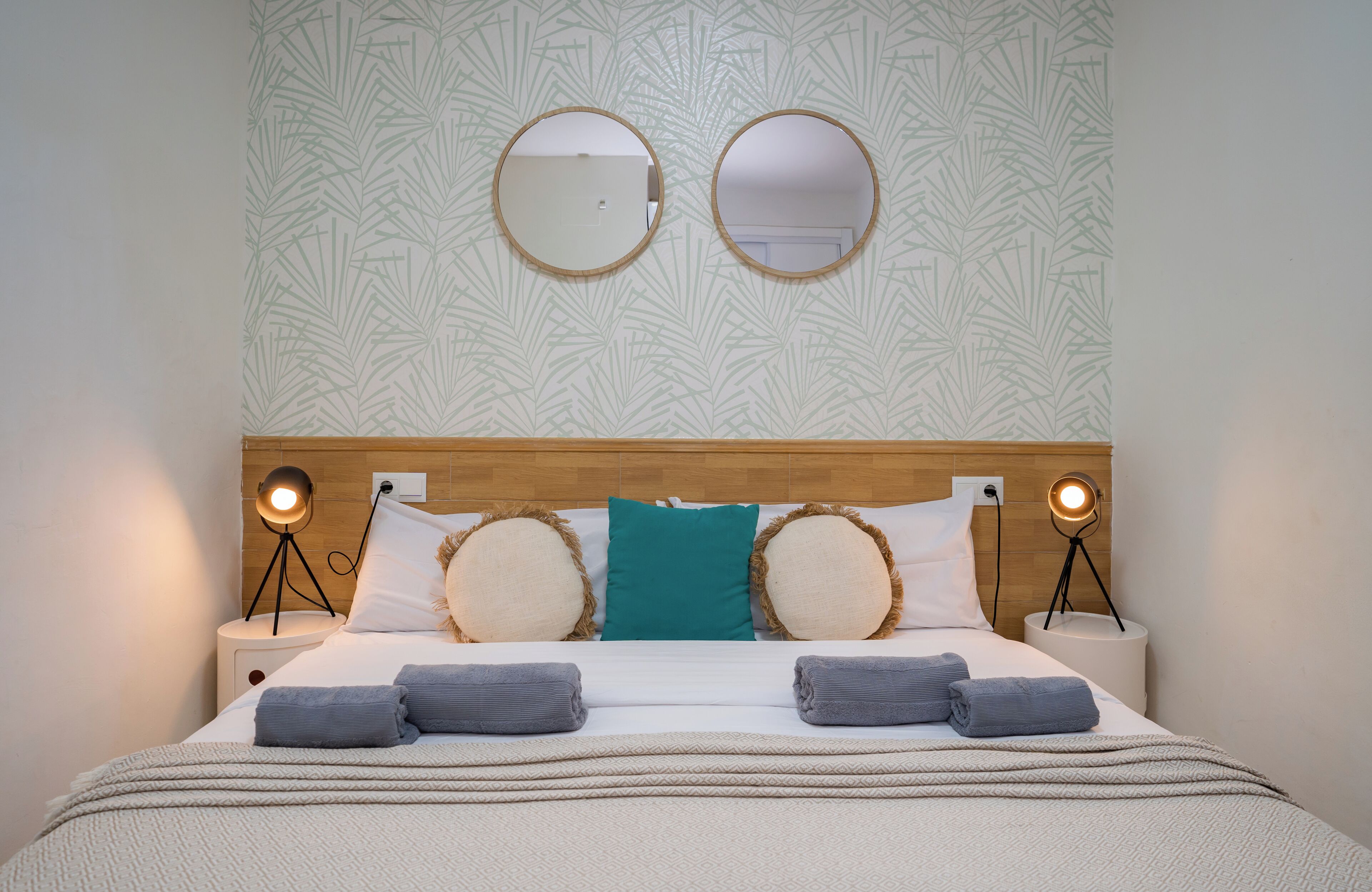 A neatly made bed with a wooden headboard, two bedside lamps, and a patterned wallpaper.