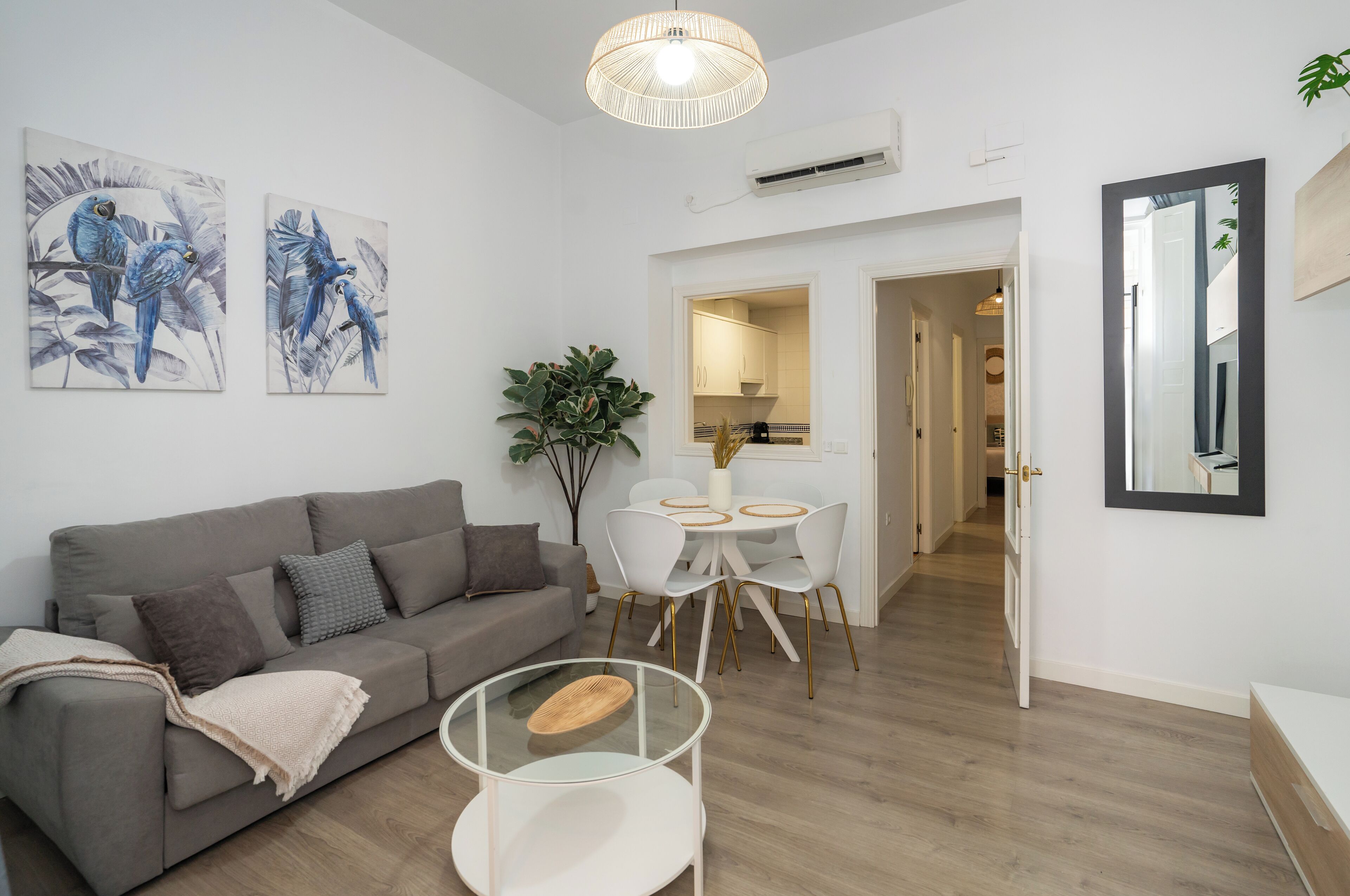 Una sala de estar moderna con un sofá gris, una mesa de centro de vidrio y dos cuadros colgados en la pared.