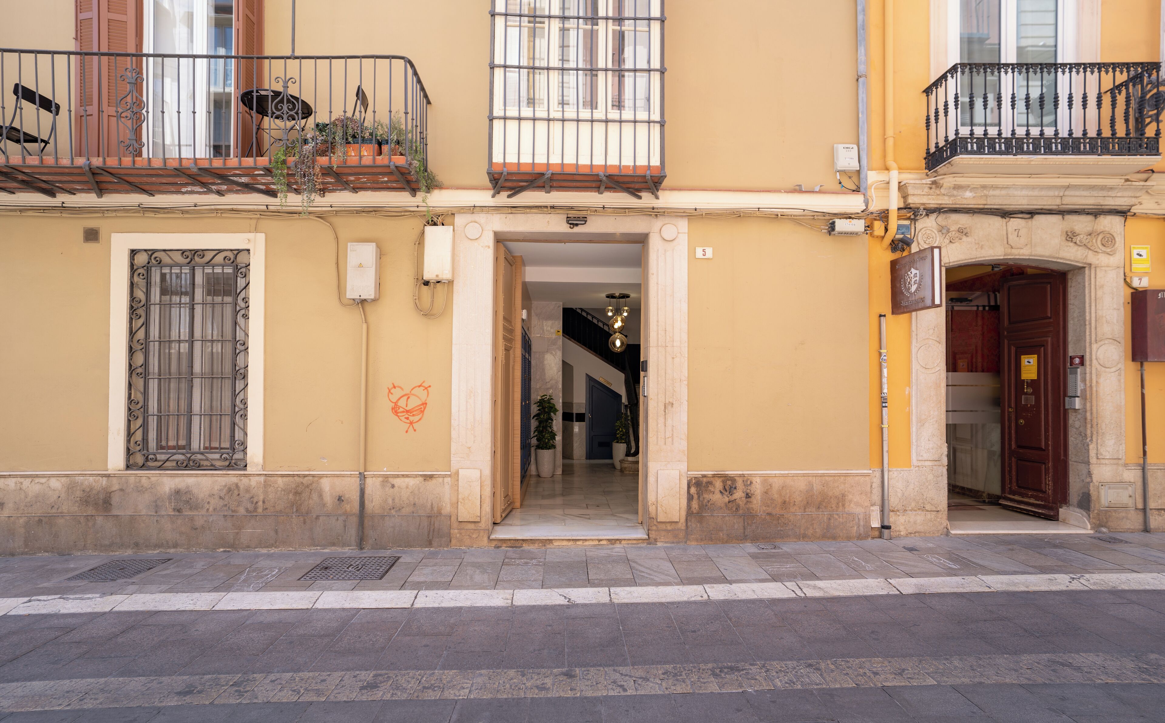 A building with a yellow facade, a wooden door, and a balcony with a metal railing.
