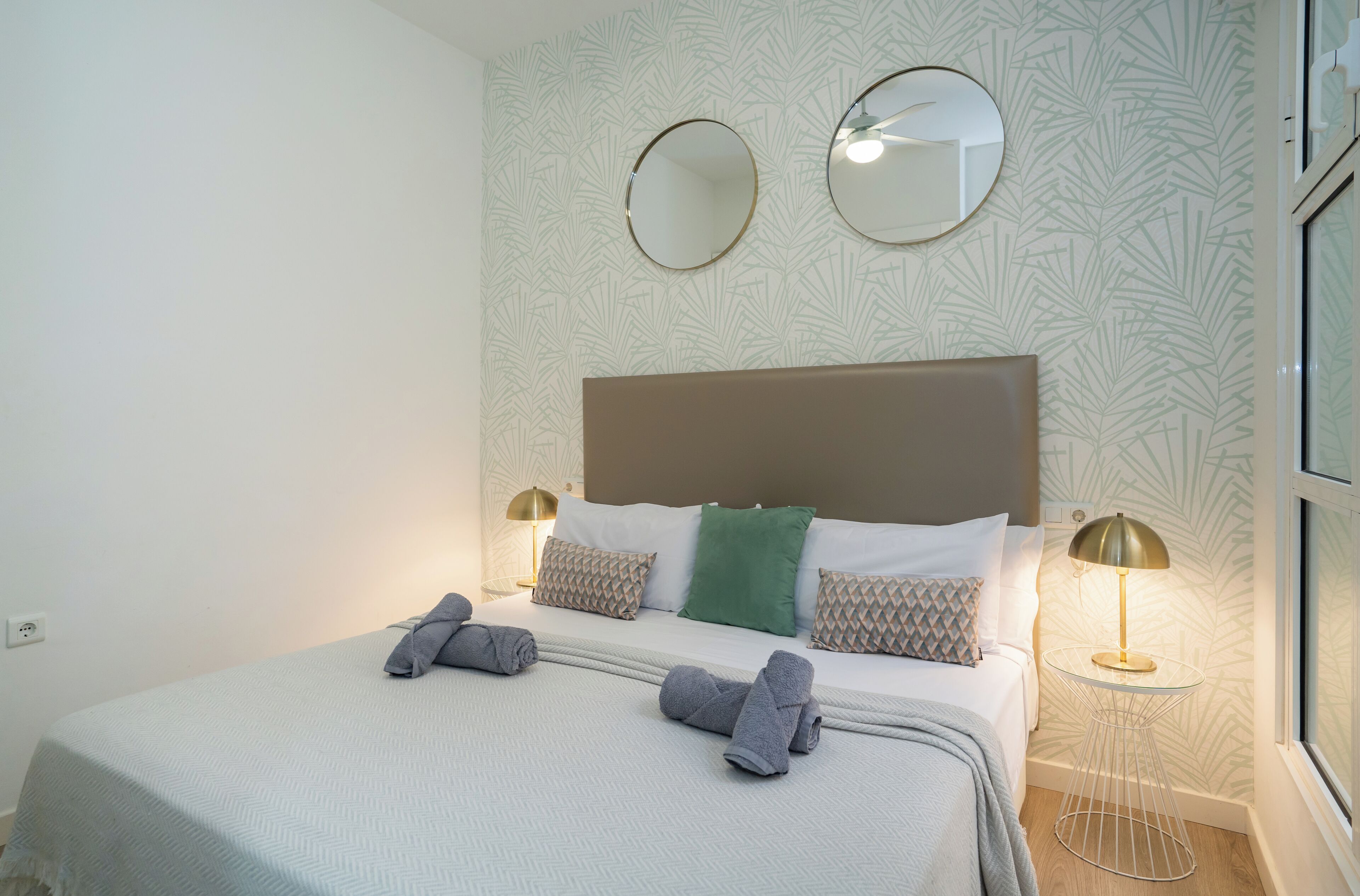 A neatly made bed with pillows and a blanket, two bedside lamps, and two wall mirrors.