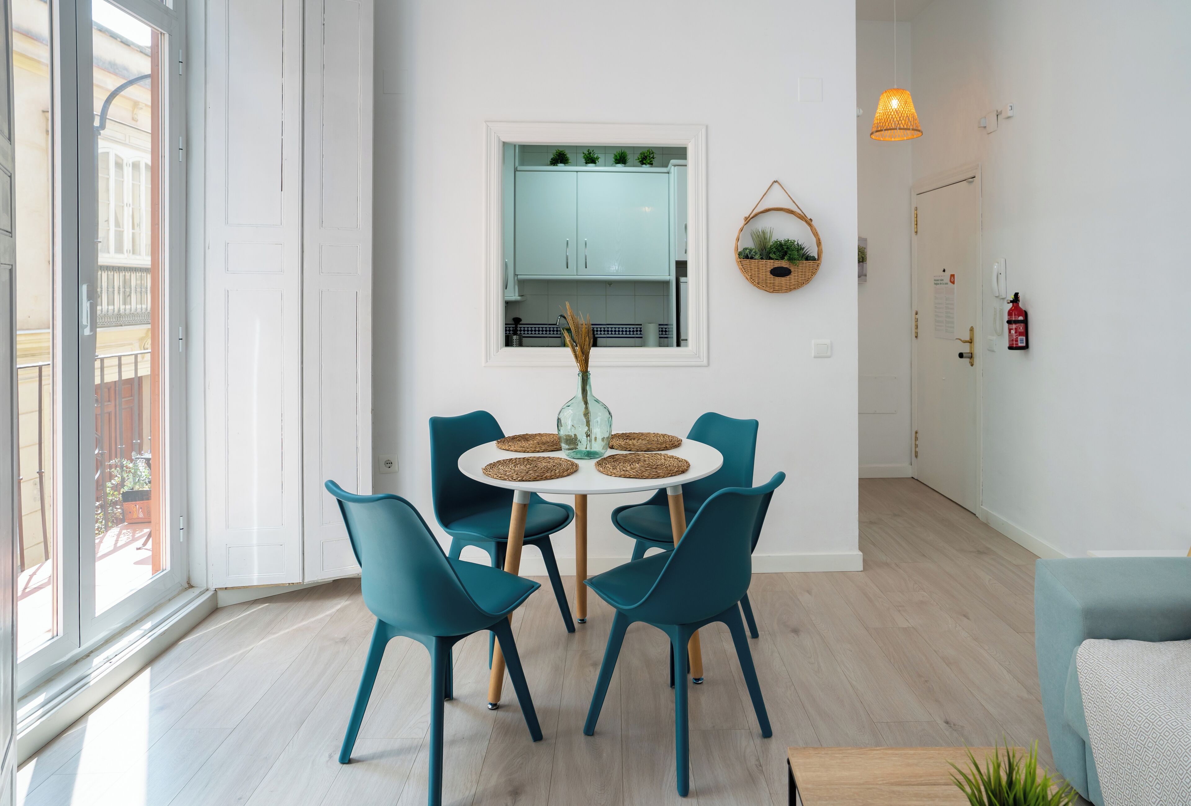 A dining area with a round table, teal chairs, and a vase with dried plants.