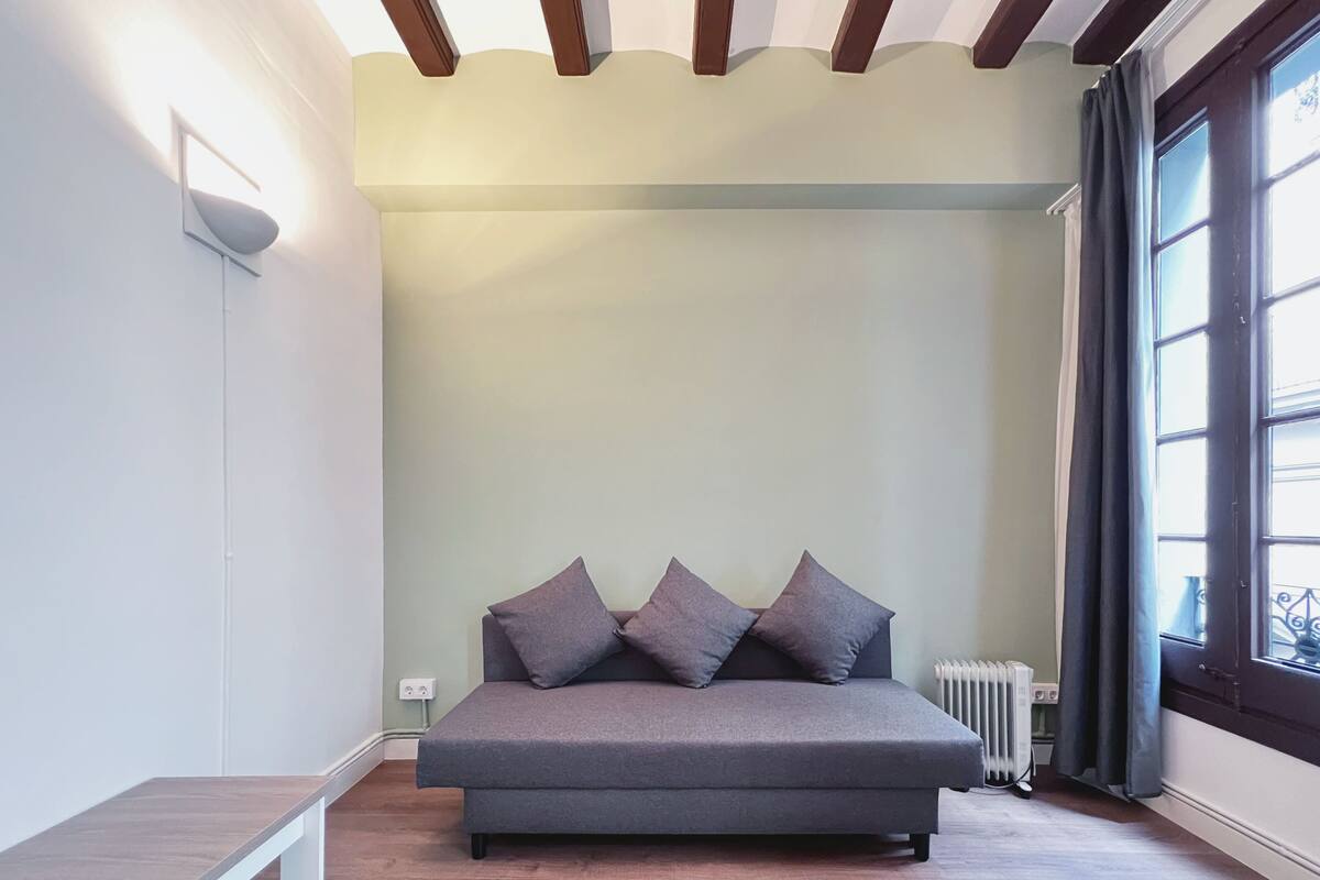 Une chambre à coucher avec un lit, un banc, un radiateur et une fenêtre avec des rideaux.