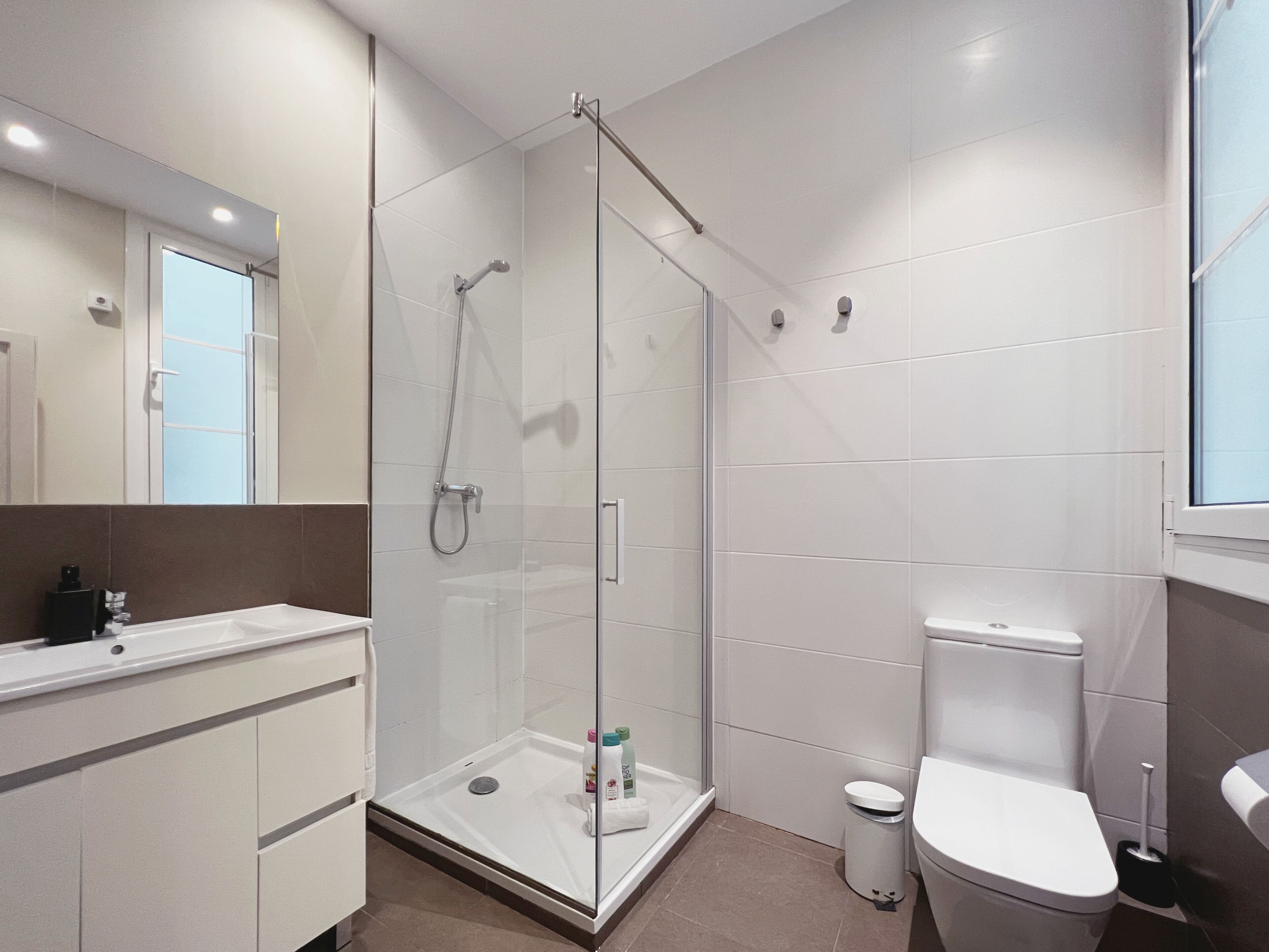 A modern bathroom with a glass-enclosed shower, a white toilet, and a vanity with a mirror.