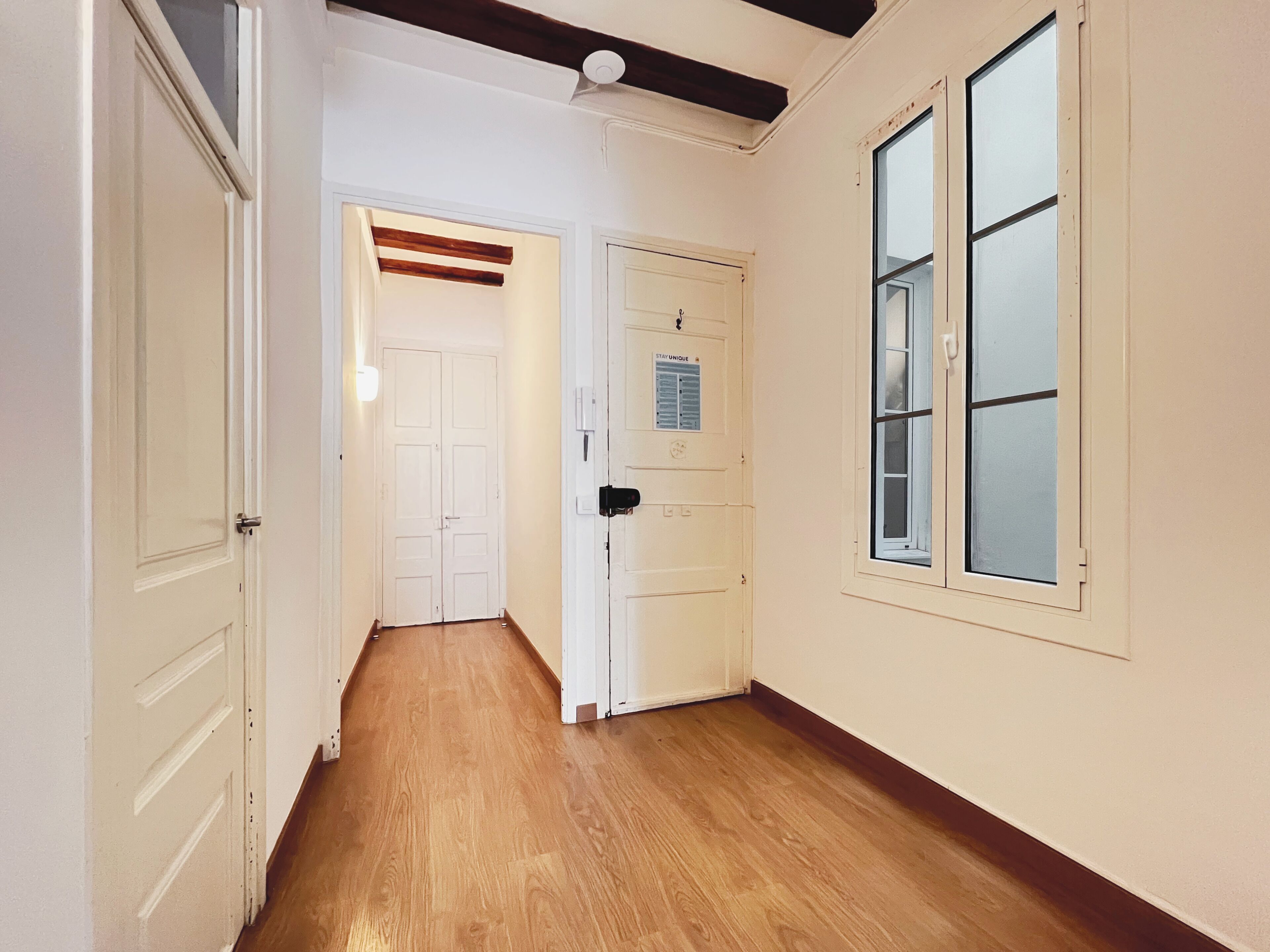 A hallway with wooden flooring, white doors, and a window with blinds.