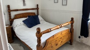 Una cama con dosel de madera con ropa de cama blanca y almohadas azules, una decoración de corazón colgada en la pared y tres láminas botánicas enmarcadas.