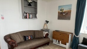 Una sala de estar con un sofá marrón, una mesita de madera, una lámpara y un cuadro en la pared.