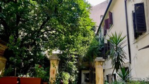 A narrow courtyard with a tiled pathway, surrounded by lush greenery and potted plants. - Detached apartment in seventeenth-century building with indoor garden. (Verona)